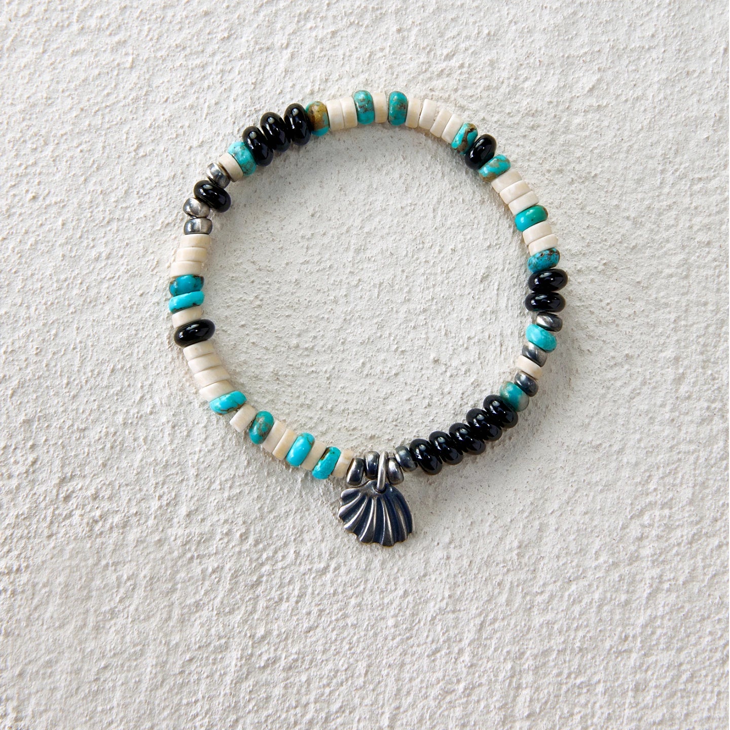 Bracelet featuring turquoise, black agate, white howlite beads and a seashell charm