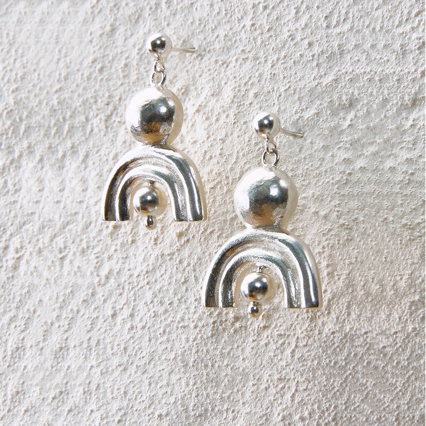 Shiny silver arc earrings with ball details, symbolizing radiance and protection
