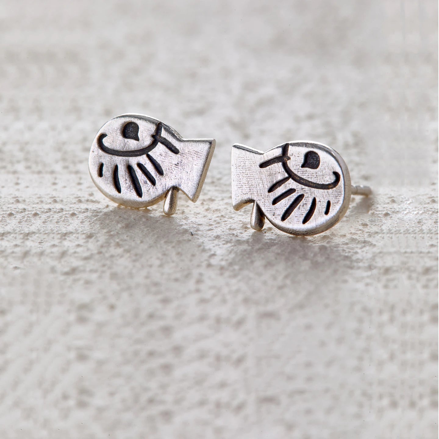 Fish-shaped silver stud earrings with engraved eyes and sunray details