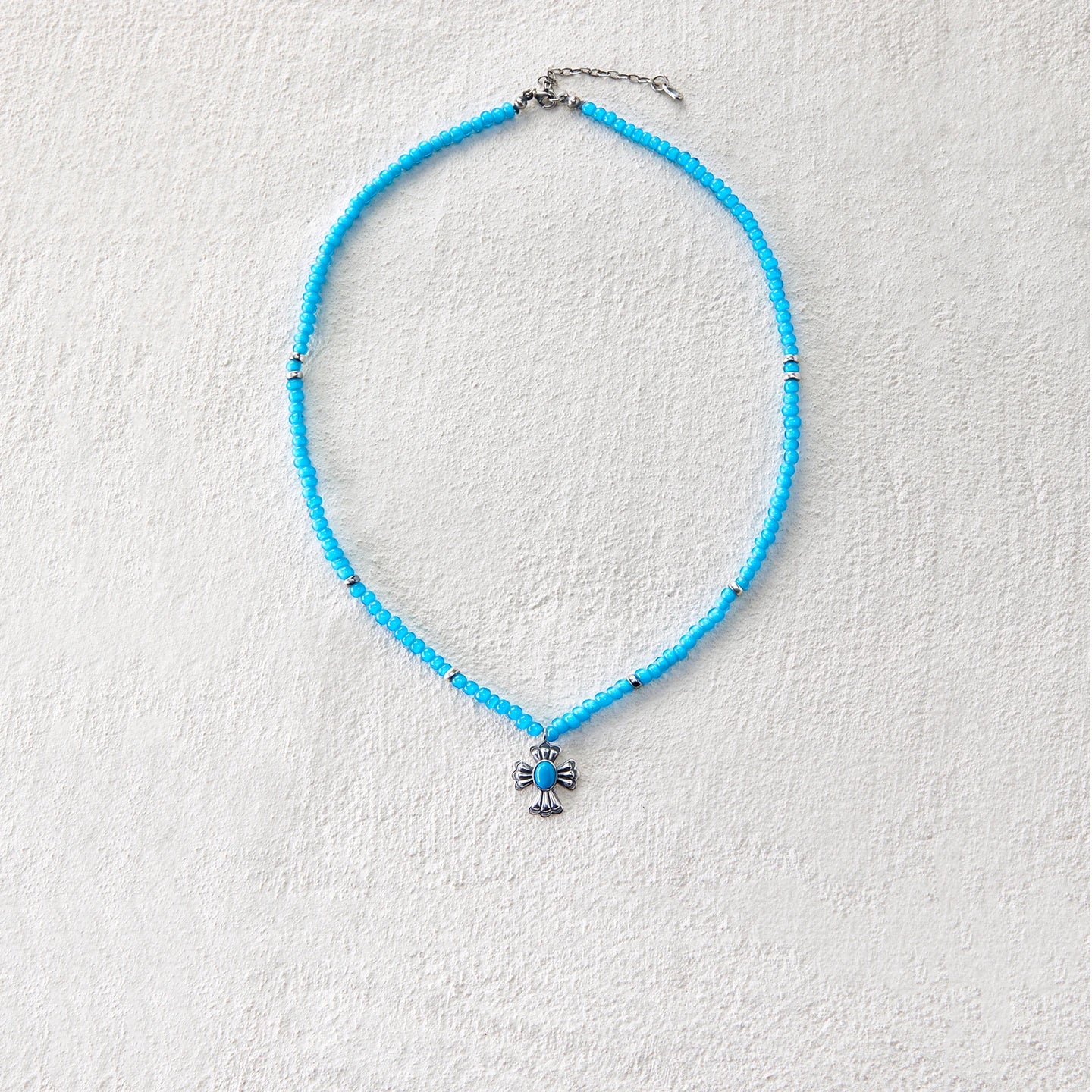 Blue glass beaded necklace with cross-shaped pendant, blending grace and mystique