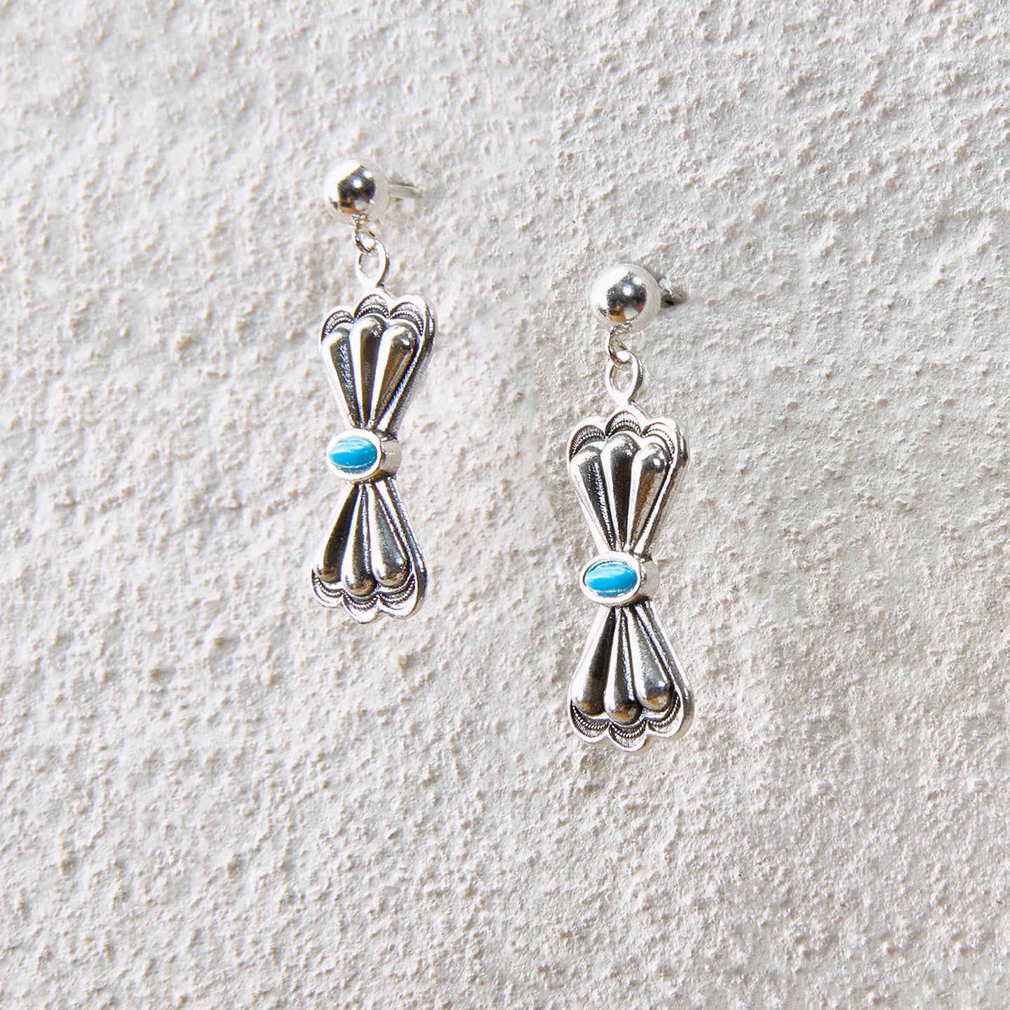 Bow-knot shaped drop earrings with turquoise accent, balancing elegance and strength